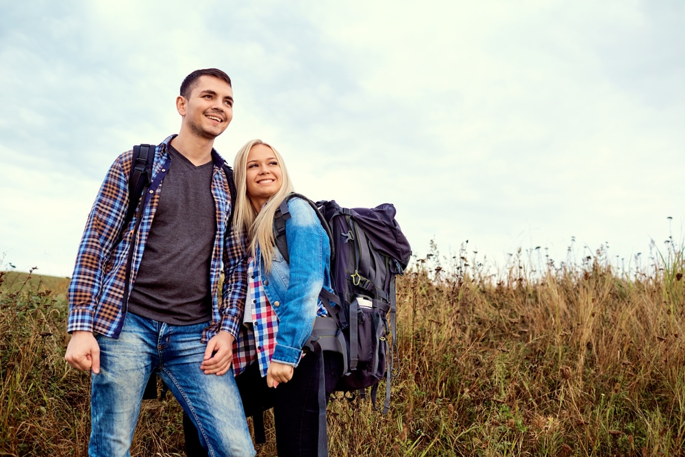 Young,Couple,Of,Tourists,With,Backpacks,On,The,Nature